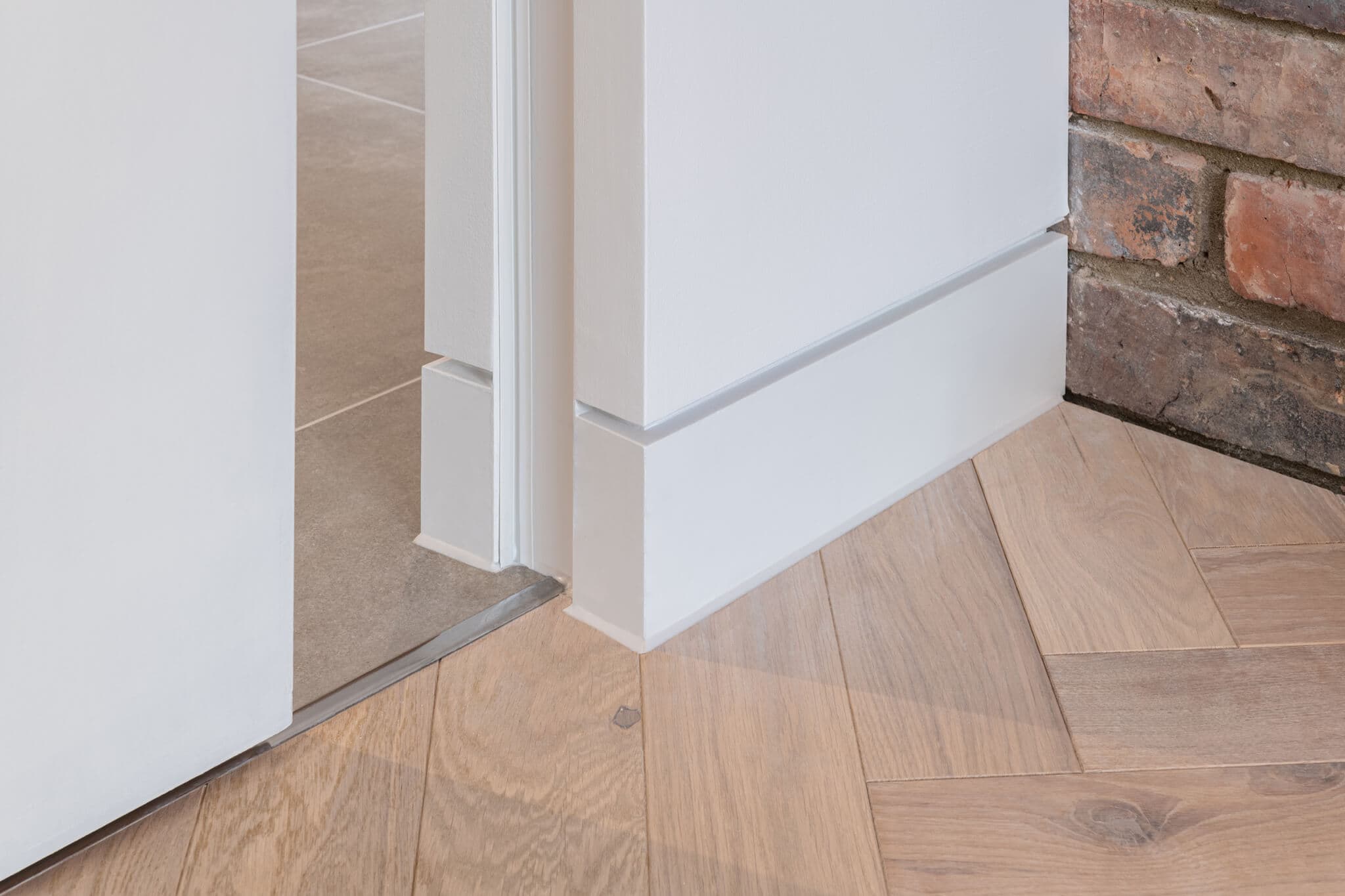 Track detail of a white sliding pocket door that is partially open, with wooden floor, brickwork and tiles.